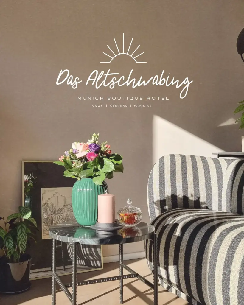Eine sonnenbeschienene Hotelecke im Boutiquehotel Das Altschwabing München ist mit einem gestreiften Sessel, einem Glastisch mit grüner Vase und rosa Kerze sowie einem Kunstwerk ausgestattet, das elegantes Grafik Design München und kreatives Visual Branding zeigt.