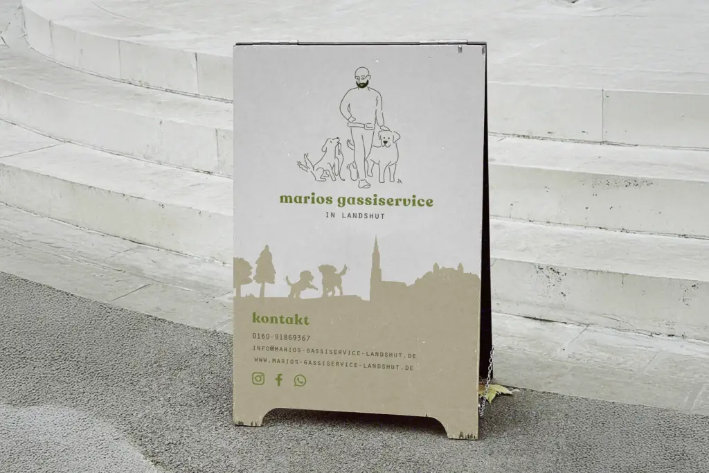 Ein Gehwegschild für marios gassierservice in Landshut mit starkem visuellen Branding und einer Stadtsilhouette zeigt einen Mann mit zwei Hunden, Kontaktinformationen und Social-Media-Symbole und ist in der Nähe von Betonstufen angebracht.