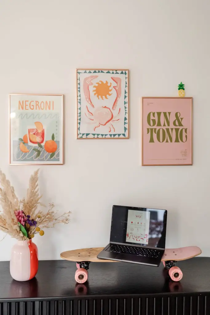 Ein schwarzer Laptop steht auf einem Skateboard auf einem schwarzen Konsolentisch und zeigt das kreative Visual Branding. Dahinter befinden sich drei gerahmte Wanddrucke und eine Vase mit Trockenblumen auf der linken Seite des Tisches.