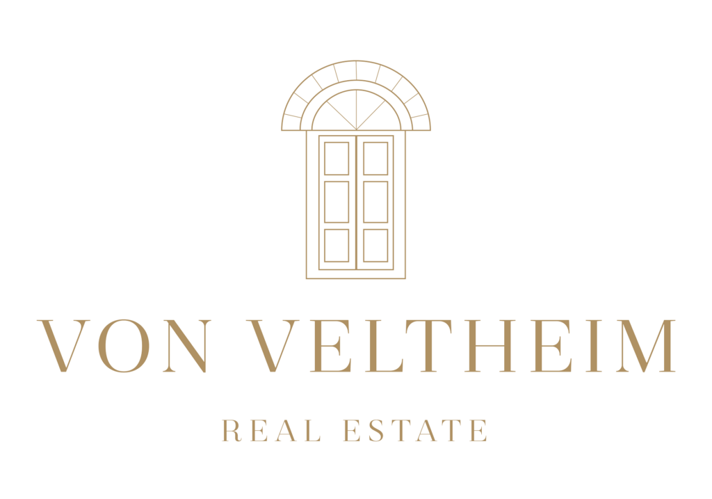 Minimalistisches Logo mit einem stilisierten Bogenfenster über "VON VELTHEIM" in eleganter Goldschrift, darunter "REAL ESTATE" - ideal für anspruchsvolles visuelles Branding und Logodesign München auf hellem Hintergrund.